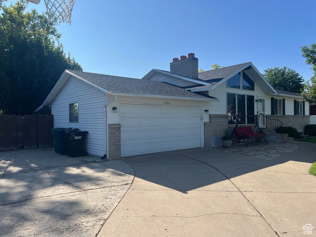 View of side of home featuring brick siding, a chimney, a garage, concrete driveway, and a shingled roof