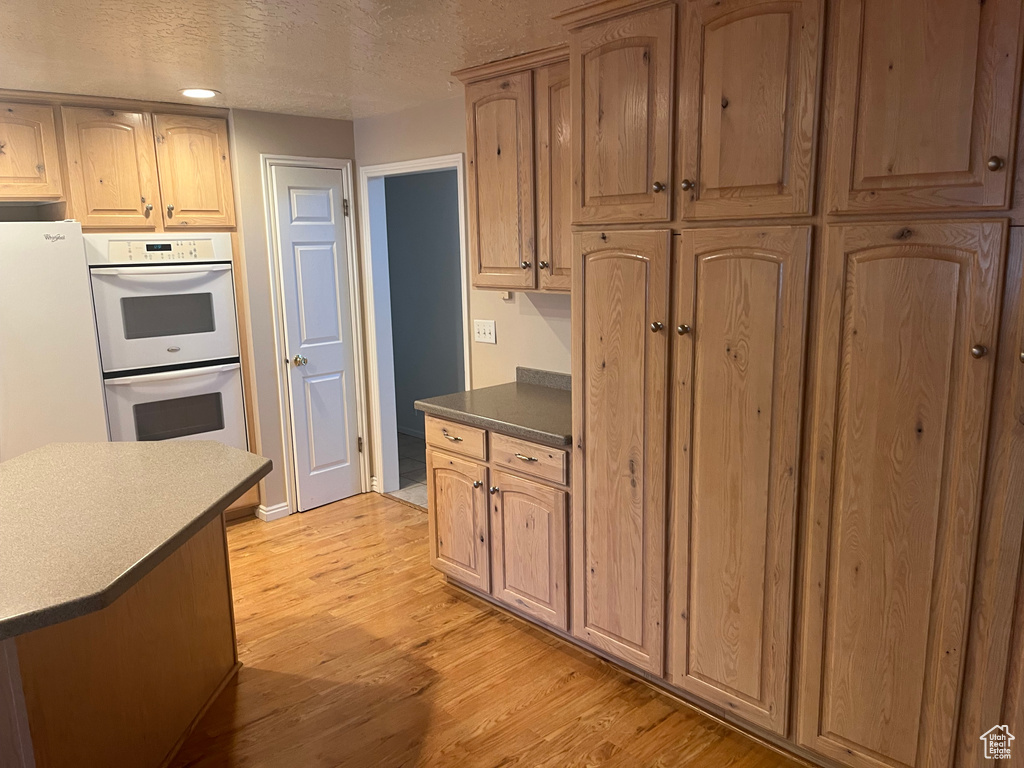 Kitchen featuring white double oven, light wood-type flooring, a textured ceiling, and dark countertops