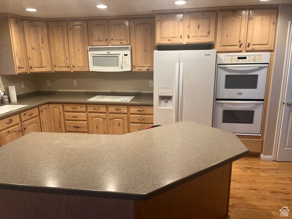 Kitchen with white appliances, light wood finished floors, recessed lighting, and dark countertops