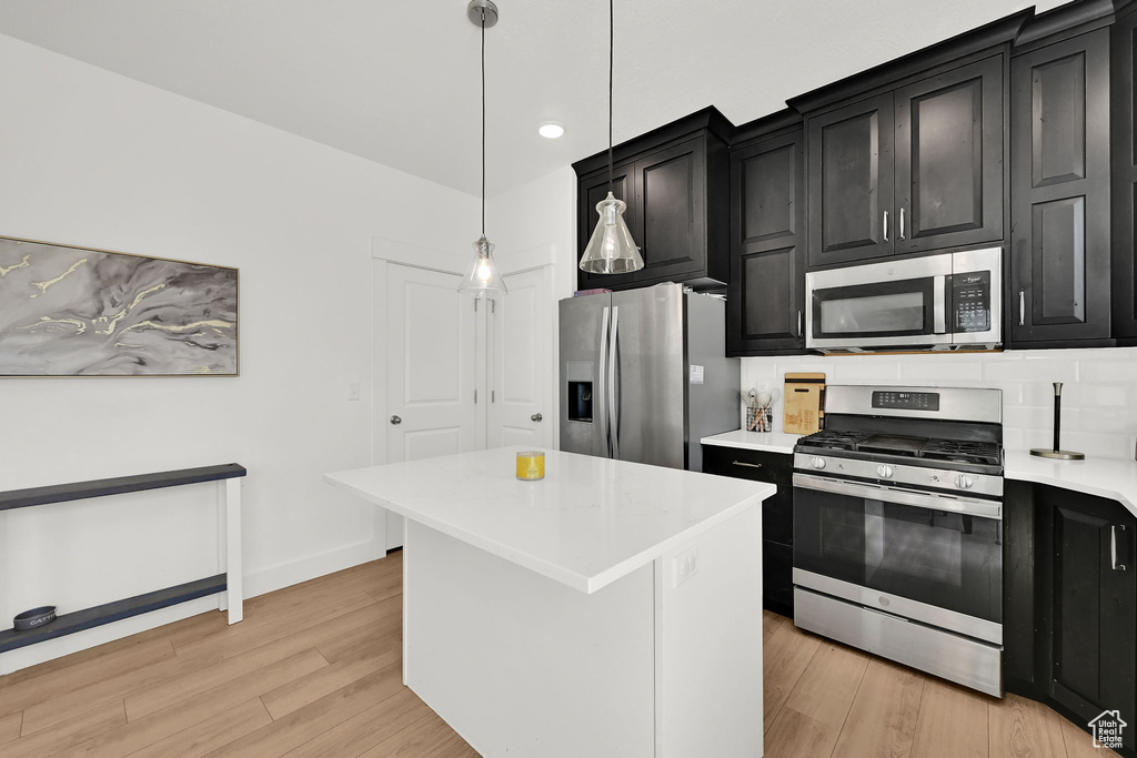 Kitchen with appliances with stainless steel finishes, dark cabinetry, light countertops, light wood-type flooring, and a center island