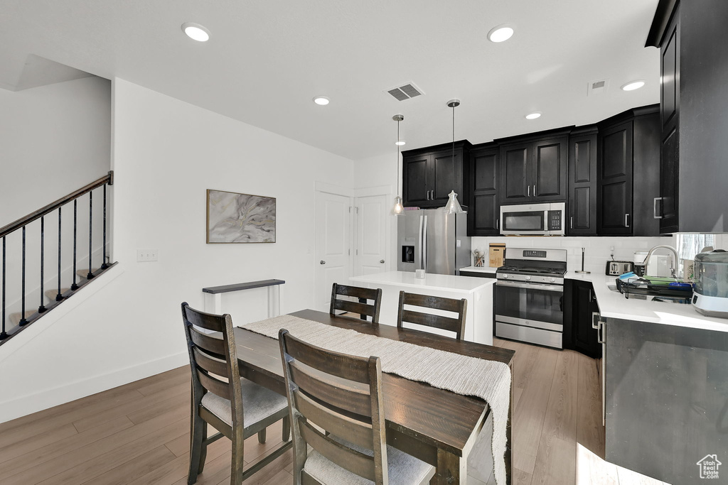 Kitchen featuring stainless steel appliances, dark cabinetry, light countertops, light wood-type flooring, and recessed lighting