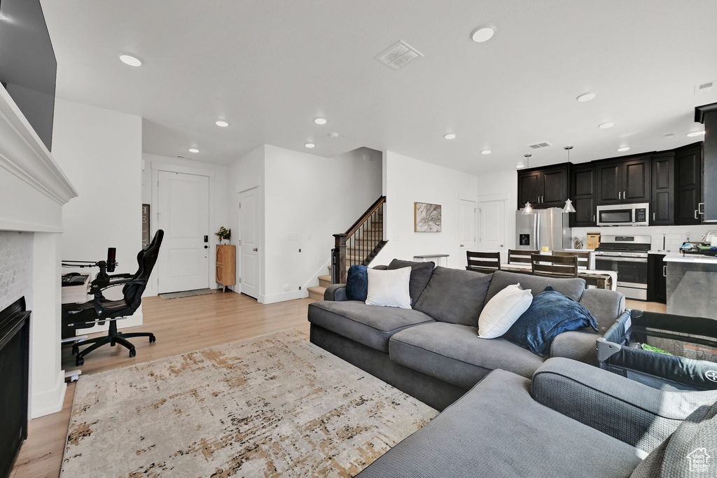 Living room with light wood-type flooring, recessed lighting, stairs, an office area, and a fireplace