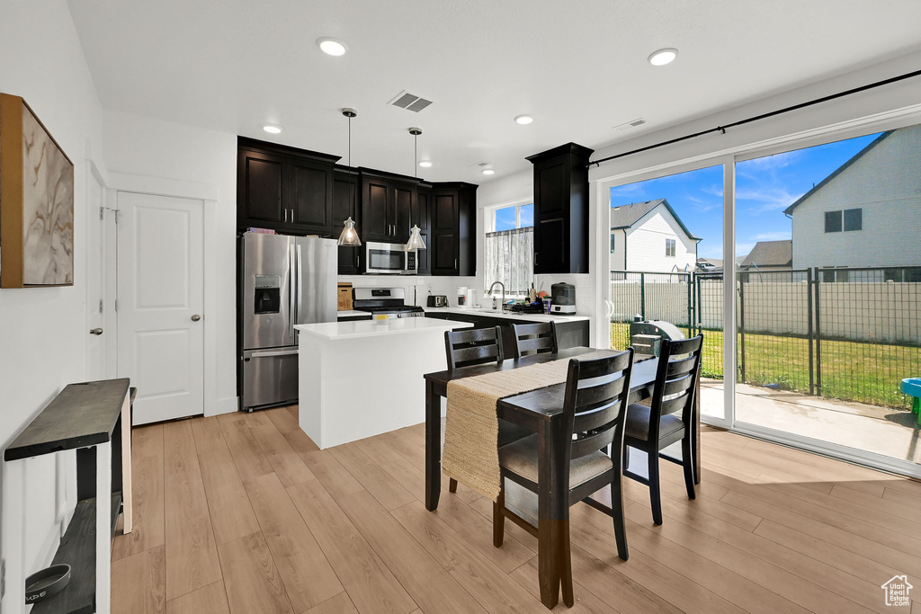 Kitchen featuring stainless steel appliances, dark cabinets, light countertops, a center island, and light wood-style flooring
