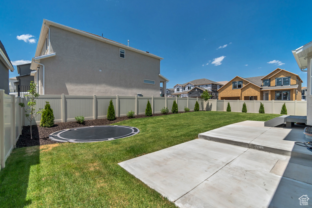 Fenced backyard featuring a trampoline, a patio area, and a residential view