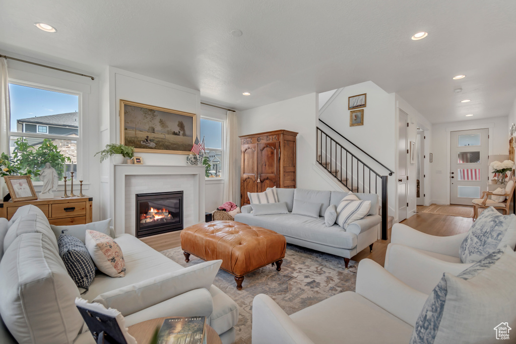 Living area featuring recessed lighting, light wood-style flooring, stairs, plenty of natural light, and a glass covered fireplace