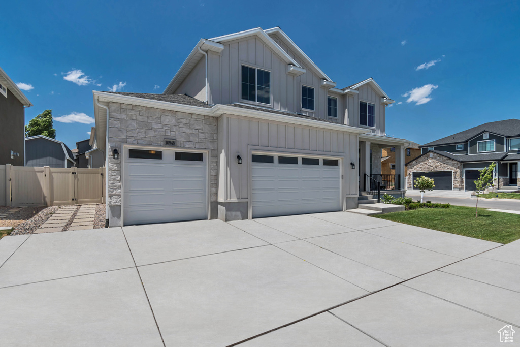 View of front facade featuring board and batten siding, stone siding, concrete driveway, a gate, and an attached garage