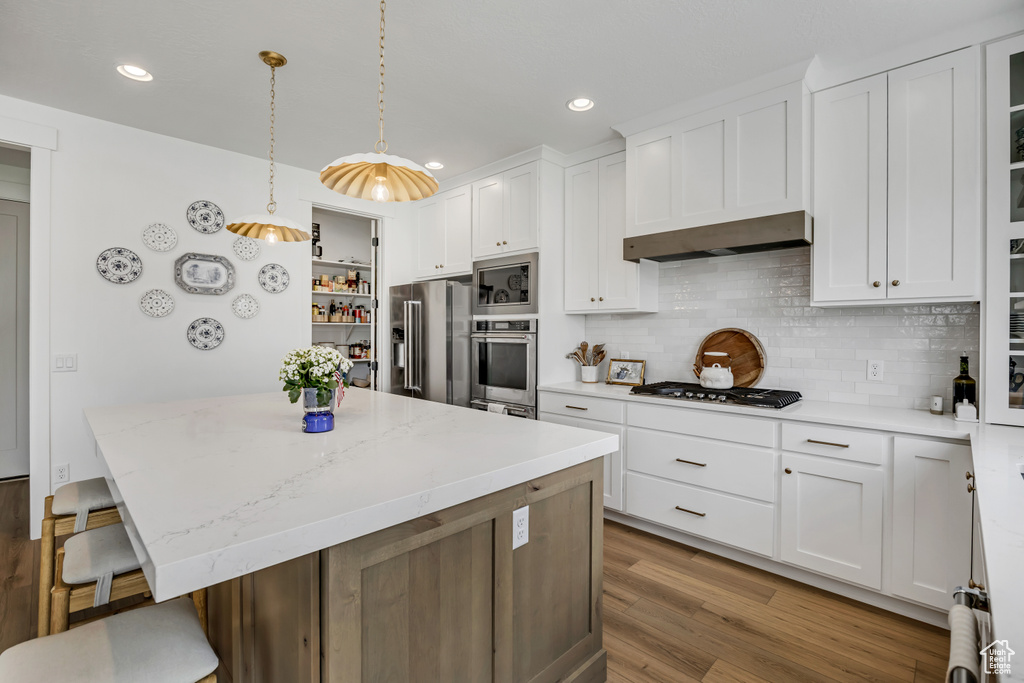 Kitchen with stainless steel appliances, a center island, under cabinet range hood, white cabinetry, and recessed lighting