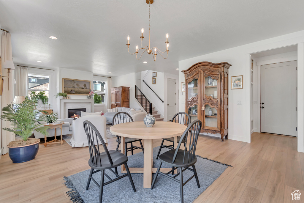 Dining space featuring stairway, light wood finished floors, a lit fireplace, recessed lighting, and a chandelier