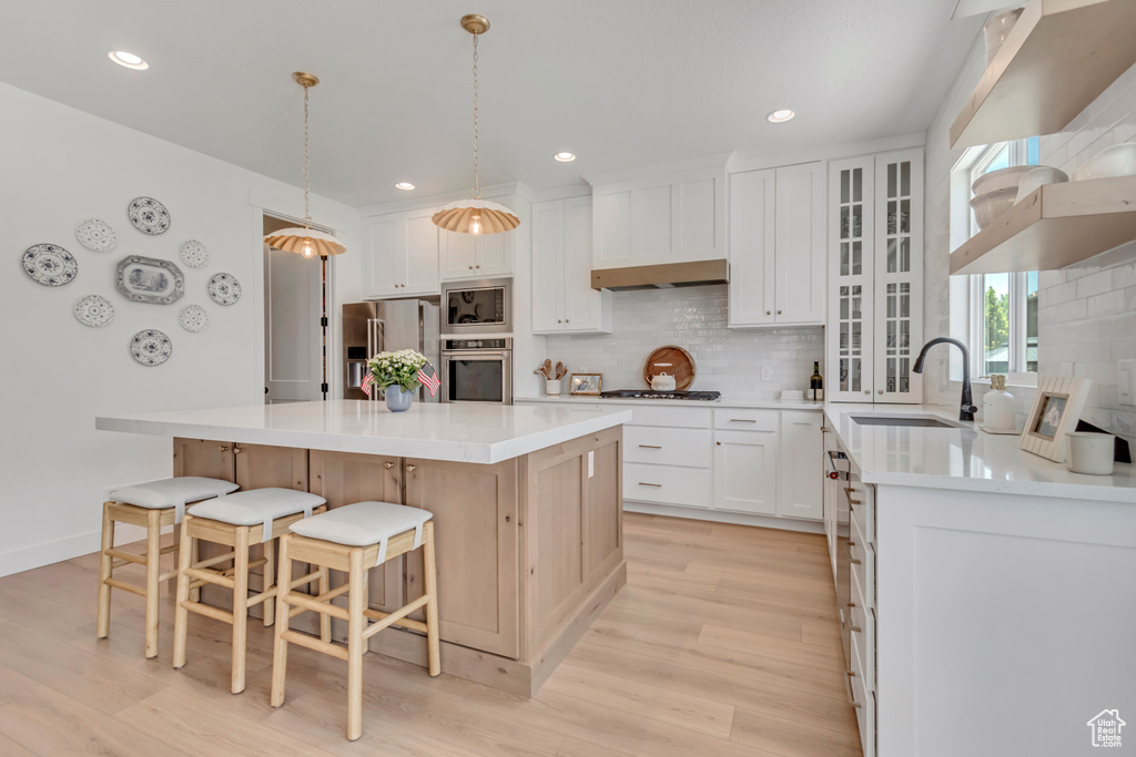 Kitchen with stainless steel appliances, light wood finished floors, backsplash, a breakfast bar, and a center island