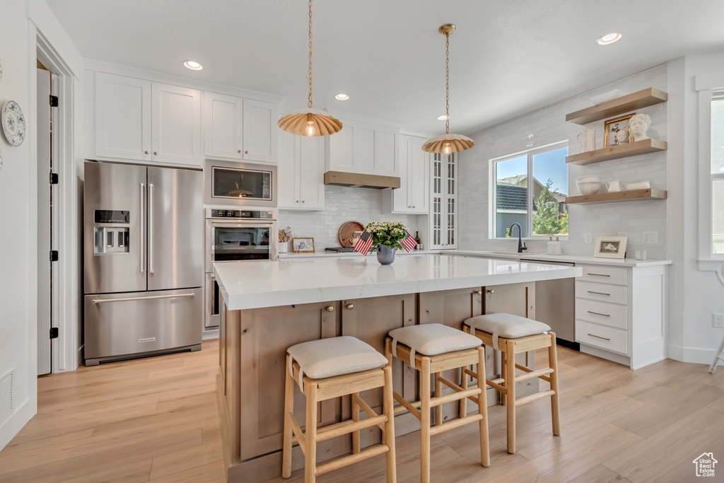 Kitchen with stainless steel appliances, backsplash, white cabinets, a breakfast bar, and recessed lighting