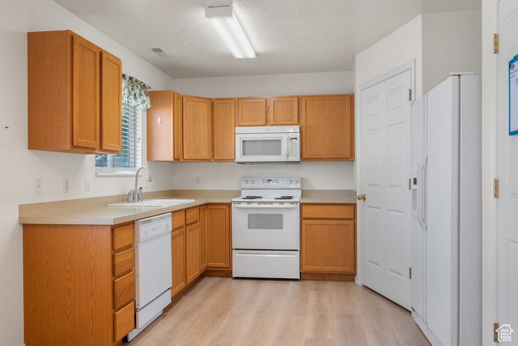 Kitchen with white appliances, light wood-style floors, and light countertops
