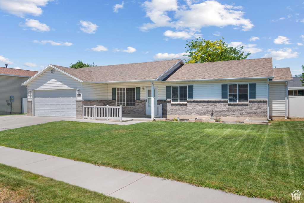 Ranch-style home with a porch, an attached garage, a front lawn, driveway, and brick siding