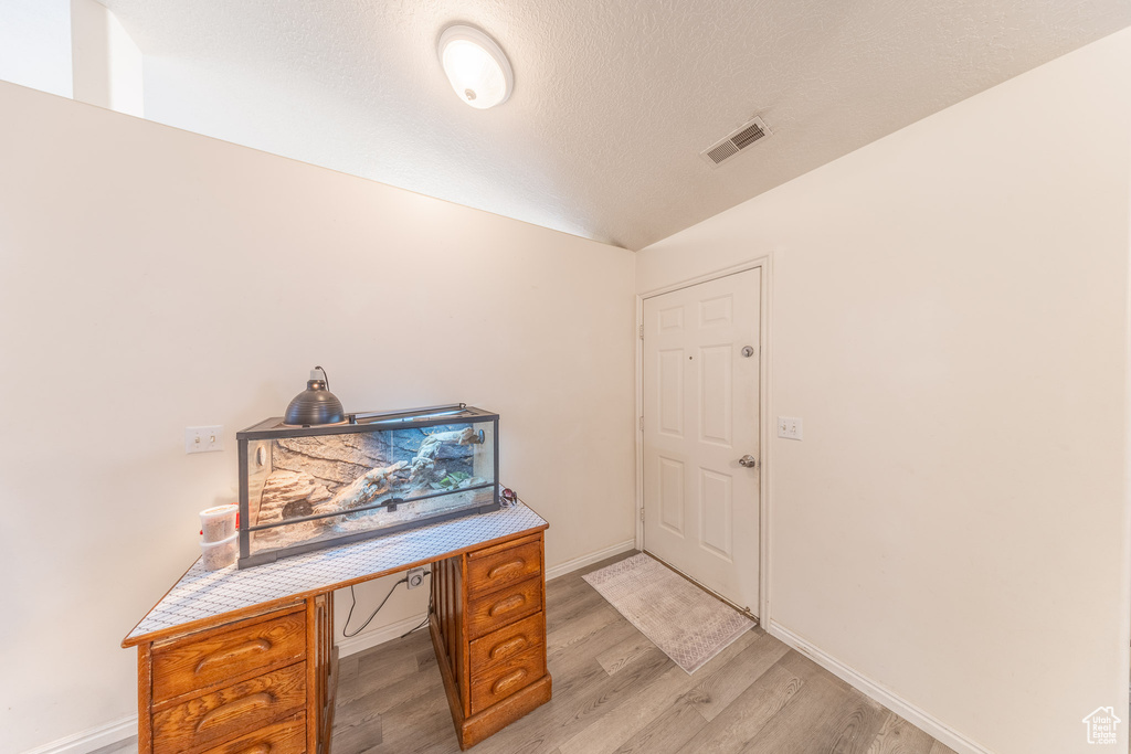 Home office featuring light wood-style floors, vaulted ceiling, and a textured ceiling