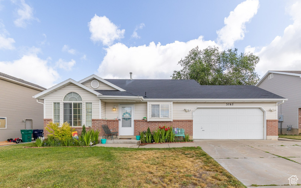 View of front facade featuring brick siding, driveway, an attached garage, and a front yard