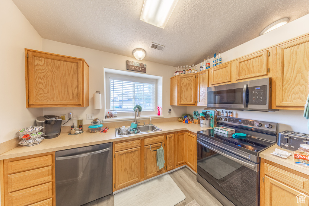 Kitchen with stainless steel appliances, light countertops, a textured ceiling, light wood finished floors, and light brown cabinets