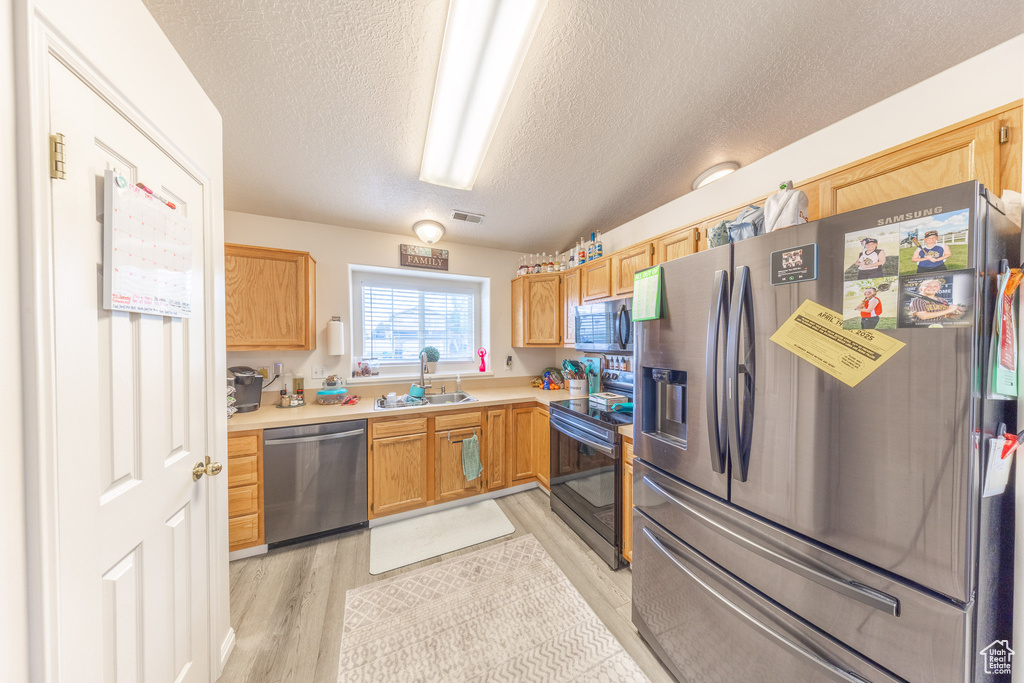 Kitchen with appliances with stainless steel finishes, a textured ceiling, light wood-style flooring, and light countertops