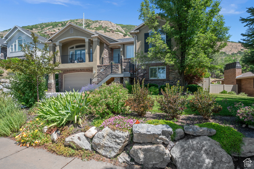 View of front facade with stone siding, stairway, a mountain view, an attached garage, and stucco siding