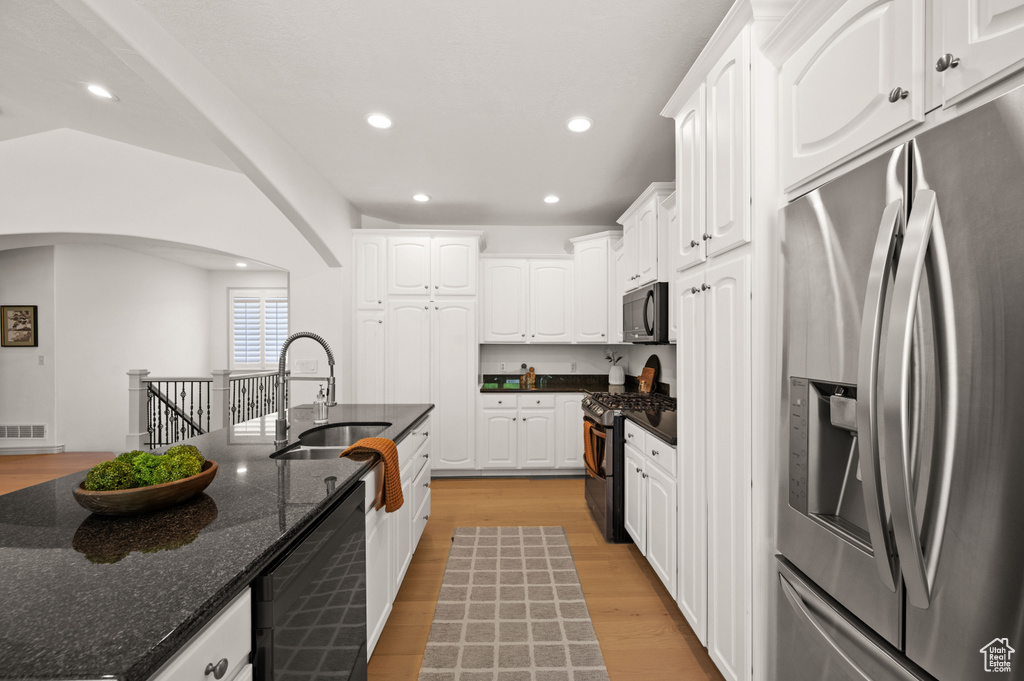 Kitchen with appliances with stainless steel finishes, white cabinetry, arched walkways, dark stone countertops, and light wood-type flooring