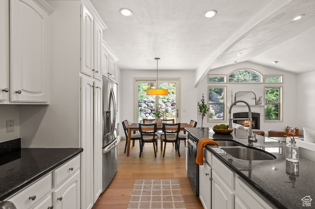 Kitchen featuring a lit fireplace, white cabinetry, stainless steel fridge, light wood-style floors, and lofted ceiling