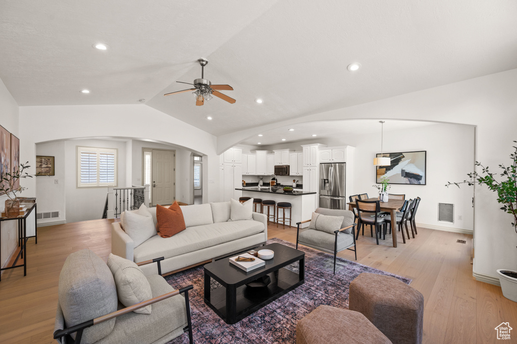 Living room with arched walkways, a ceiling fan, lofted ceiling, light wood-type flooring, and recessed lighting