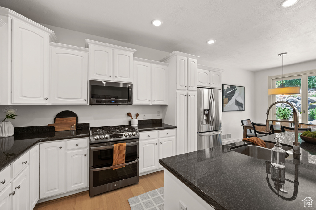 Kitchen with appliances with stainless steel finishes, recessed lighting, white cabinets, decorative light fixtures, and light wood-style flooring