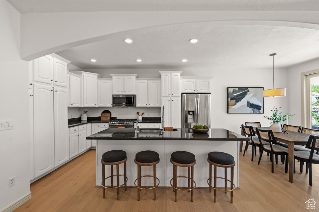 Kitchen with appliances with stainless steel finishes, white cabinets, light wood-type flooring, recessed lighting, and dark countertops