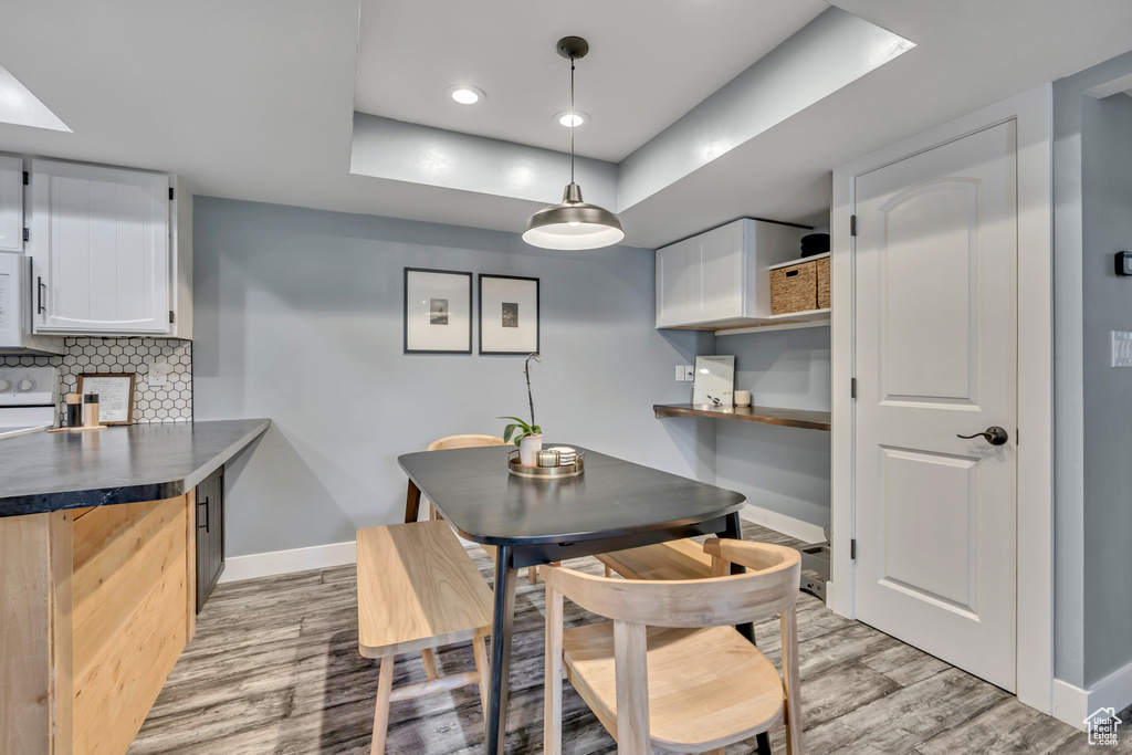 Dining room with a raised ceiling, light wood finished floors, and recessed lighting