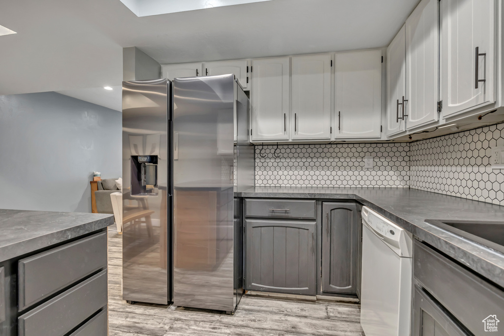 Kitchen featuring dishwasher, stainless steel fridge, dark countertops, decorative backsplash, and recessed lighting