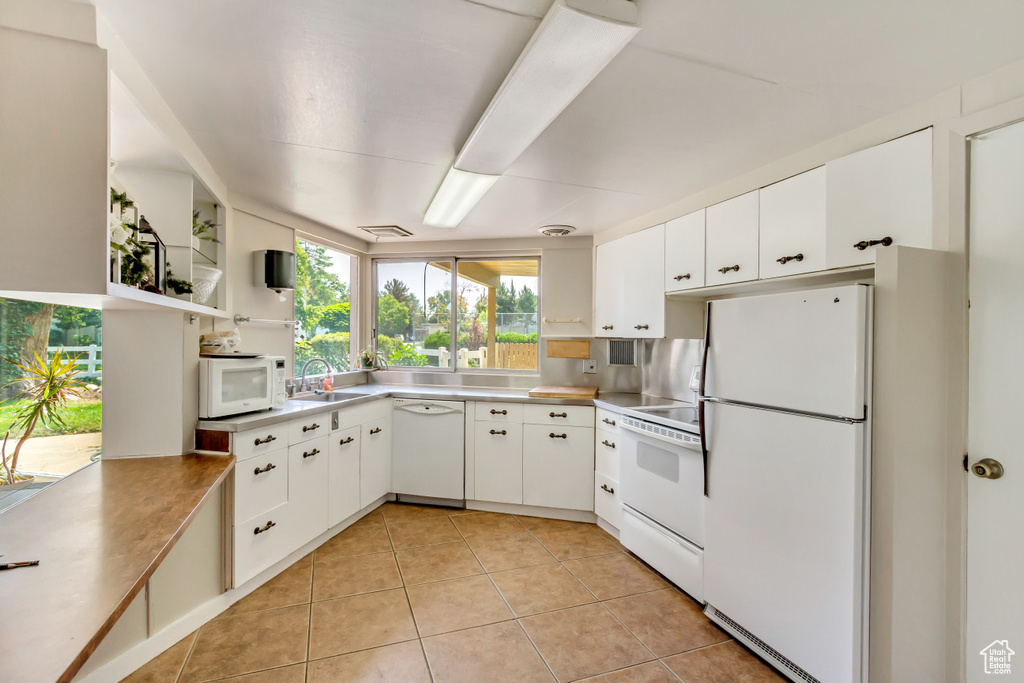 Kitchen with white appliances, light tile patterned flooring, white cabinets, and light countertops