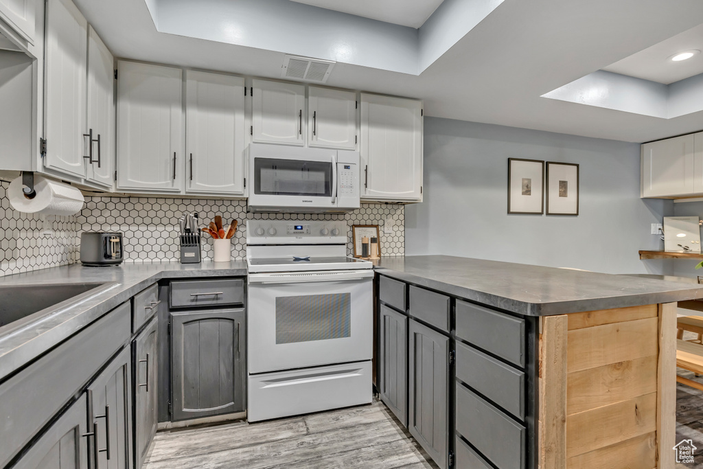 Kitchen featuring white appliances, a peninsula, gray cabinets, a raised ceiling, and light wood-type flooring