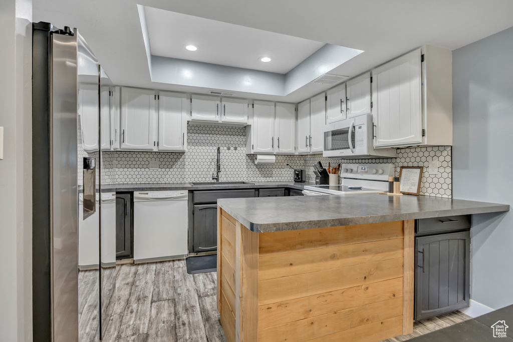 Kitchen with white appliances, a peninsula, light wood-type flooring, a raised ceiling, and decorative backsplash