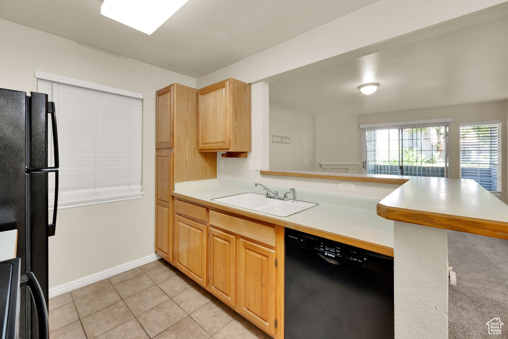 Kitchen featuring black appliances, a peninsula, light countertops, light tile patterned floors, and light brown cabinetry