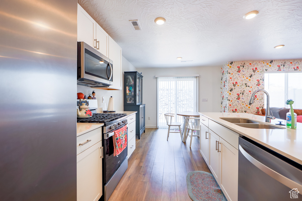 Kitchen featuring appliances with stainless steel finishes, light countertops, white cabinetry, light wood-type flooring, and recessed lighting