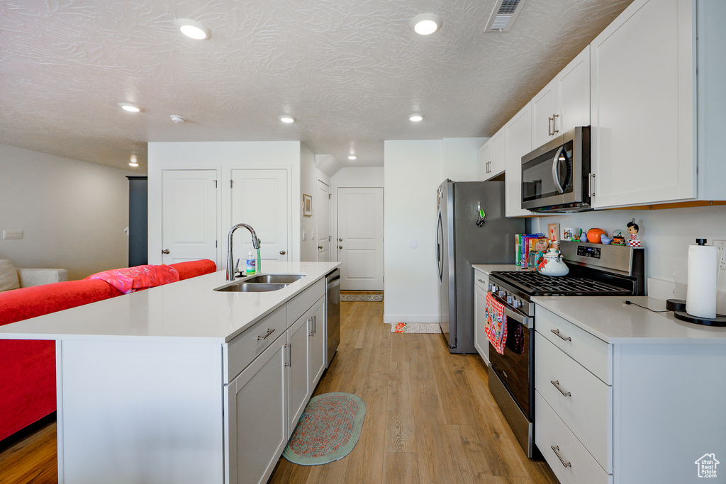 Kitchen with stainless steel appliances, light countertops, light wood-type flooring, a kitchen island with sink, and recessed lighting