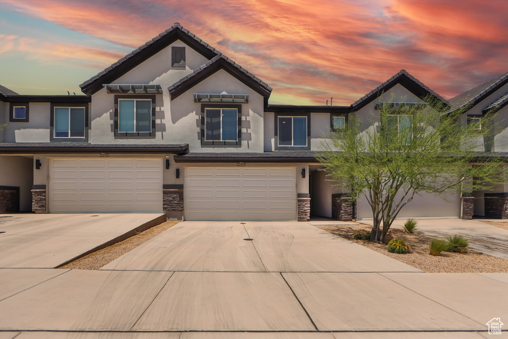 View of front facade featuring stucco siding, stone siding, an attached garage, and concrete driveway