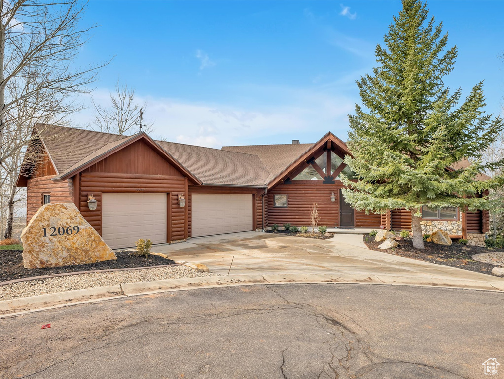 Log-style house with roof with shingles, an attached garage, and concrete driveway