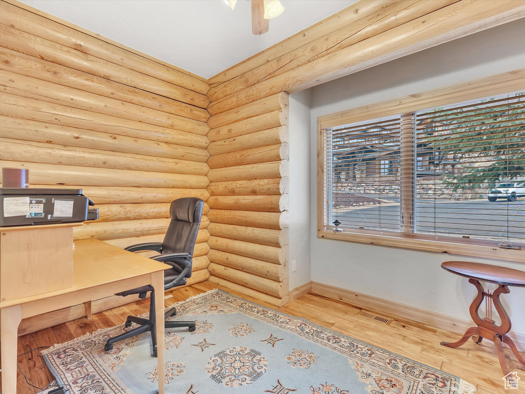 Home office with wood finished floors, log walls, and a ceiling fan