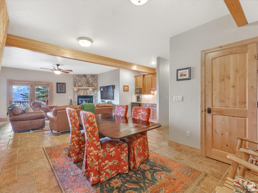 Dining space with stone tile flooring, beamed ceiling, a ceiling fan, and a fireplace