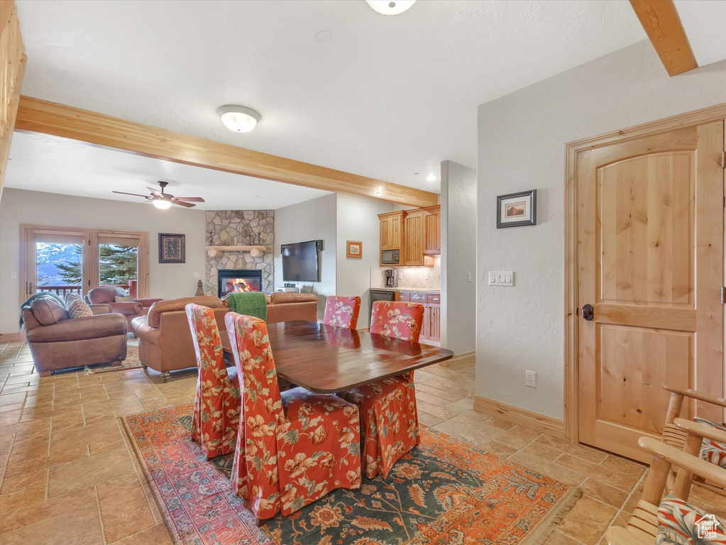 Dining room with stone tile floors, beamed ceiling, ceiling fan, and a stone fireplace