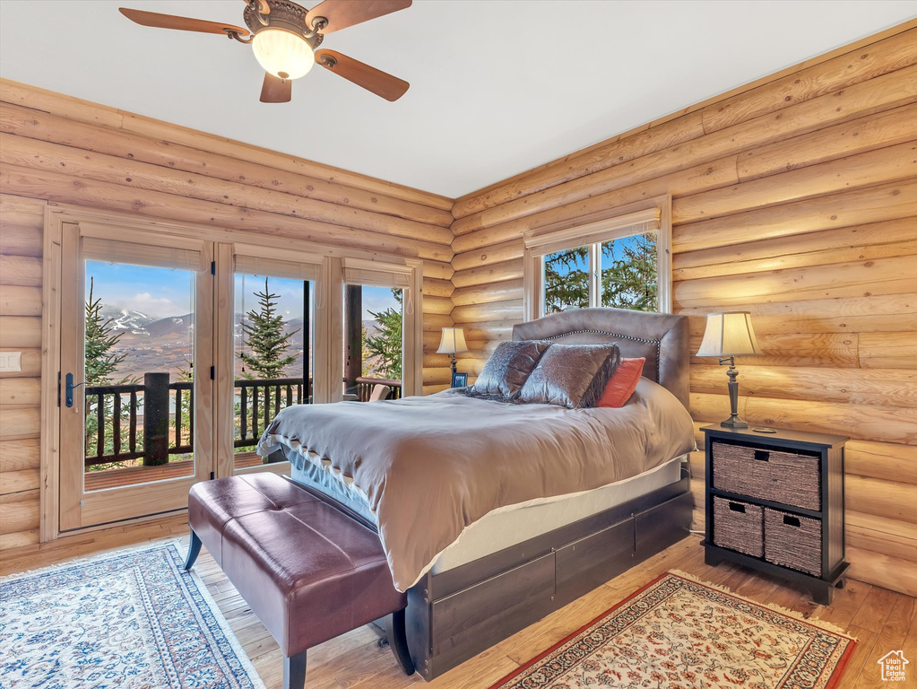 Bedroom featuring access to outside, hardwood / wood-style floors, rustic walls, and a ceiling fan