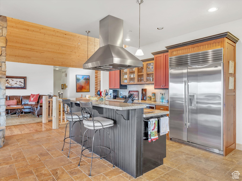 Kitchen with stainless steel built in fridge, island exhaust hood, a breakfast bar, light stone finish flooring, and recessed lighting
