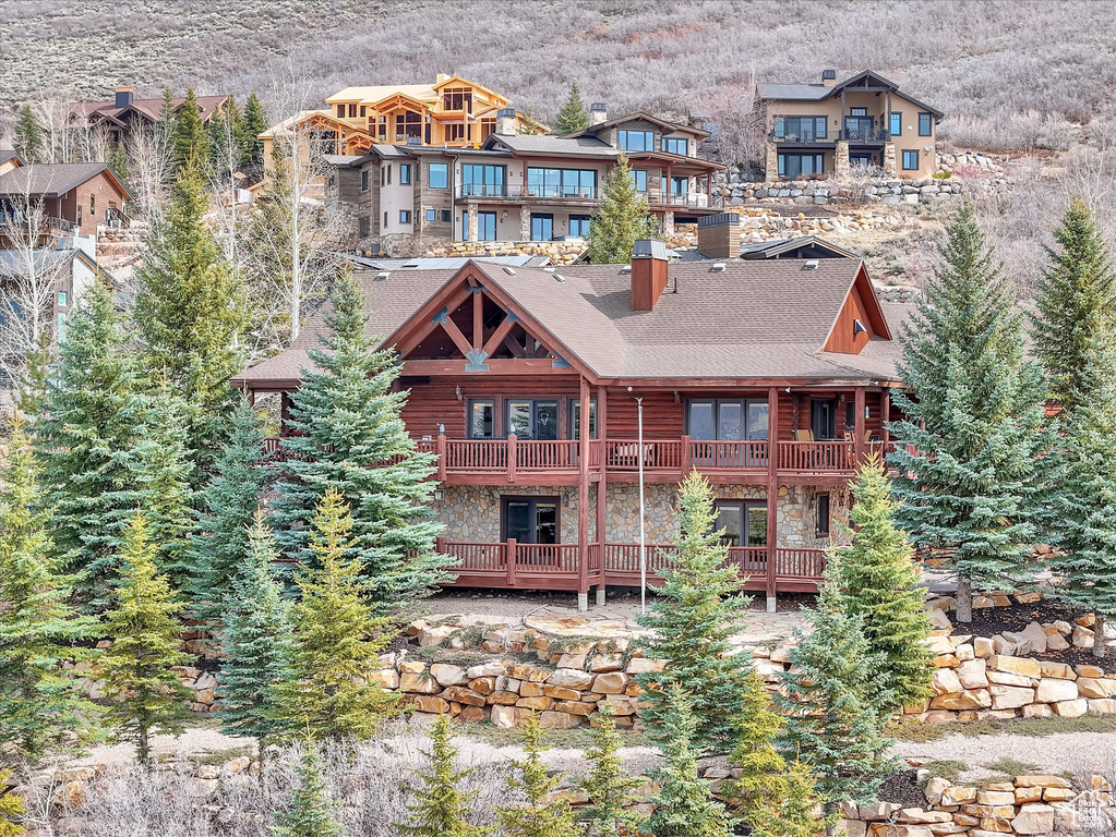 Back of house with a balcony, a mountain view, stone siding, a chimney, and a shingled roof