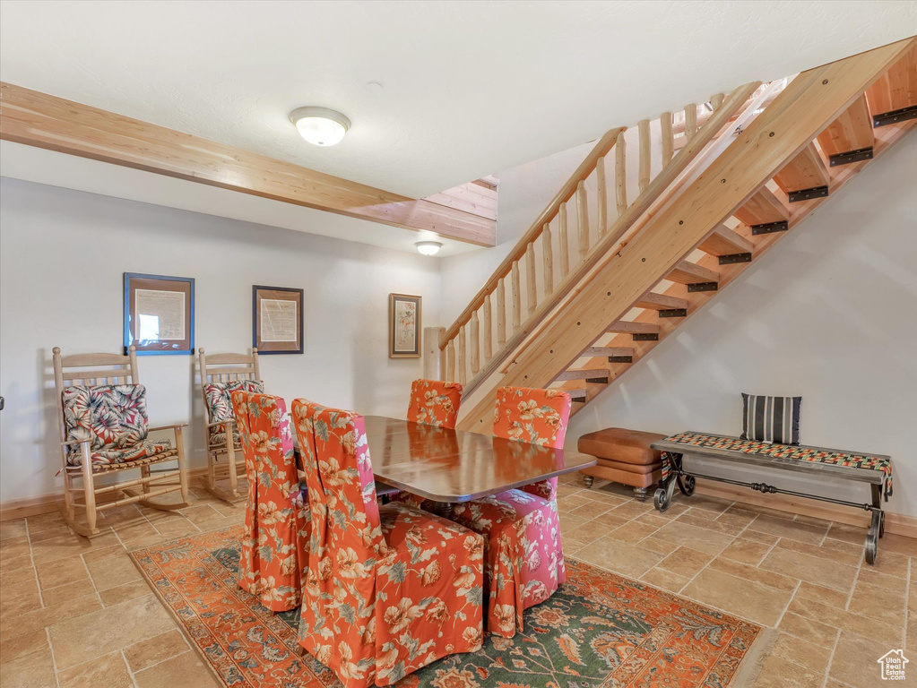 Dining area featuring stone tile floors, stairway, and beam ceiling