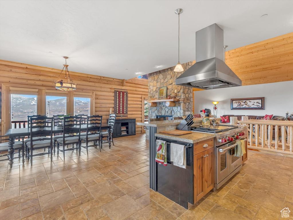 Kitchen featuring island range hood, range with two ovens, rustic walls, stone tile flooring, and a fireplace
