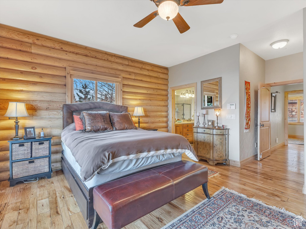 Bedroom featuring light wood finished floors, connected bathroom, log walls, and ceiling fan