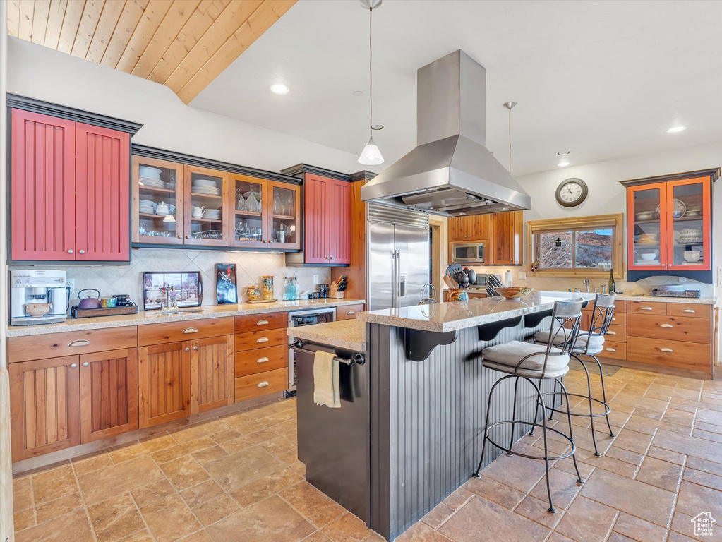 Kitchen with island range hood, built in appliances, stone tile floors, tasteful backsplash, and recessed lighting