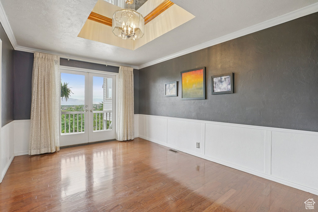 Empty room with a chandelier, french doors, ornamental molding, wainscoting, and wood finished floors