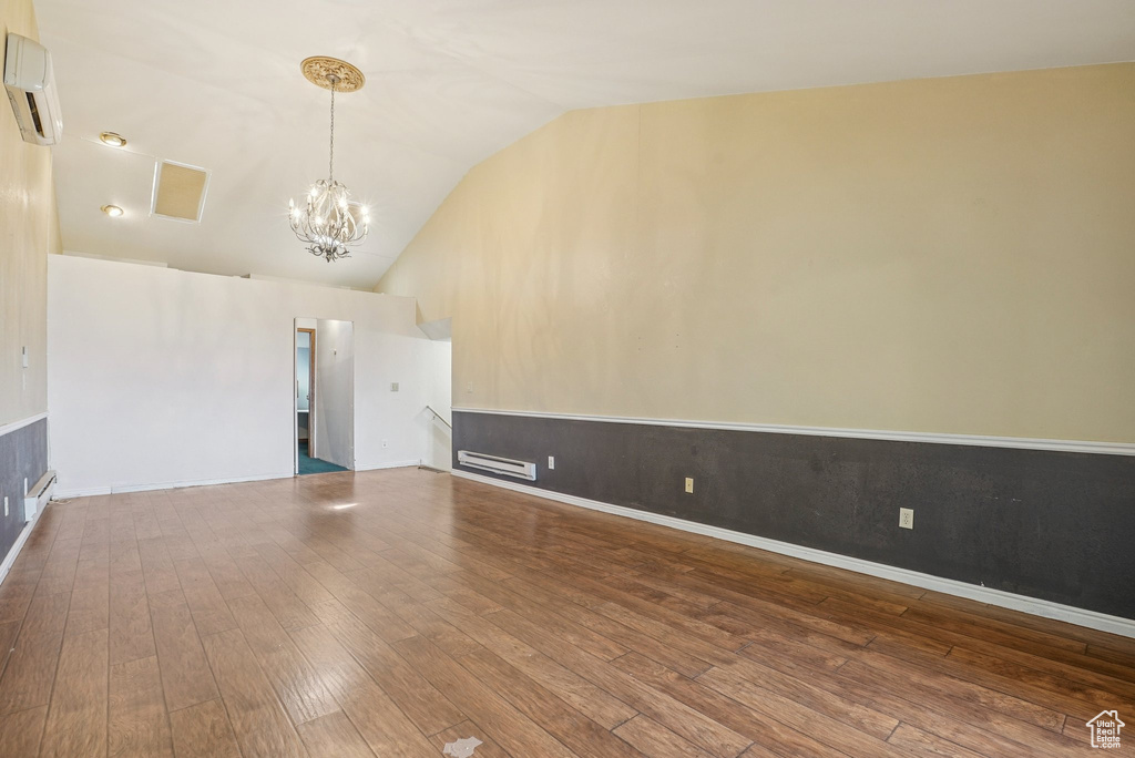 Unfurnished living room featuring a wall unit AC, a chandelier, hardwood / wood-style flooring, and vaulted ceiling