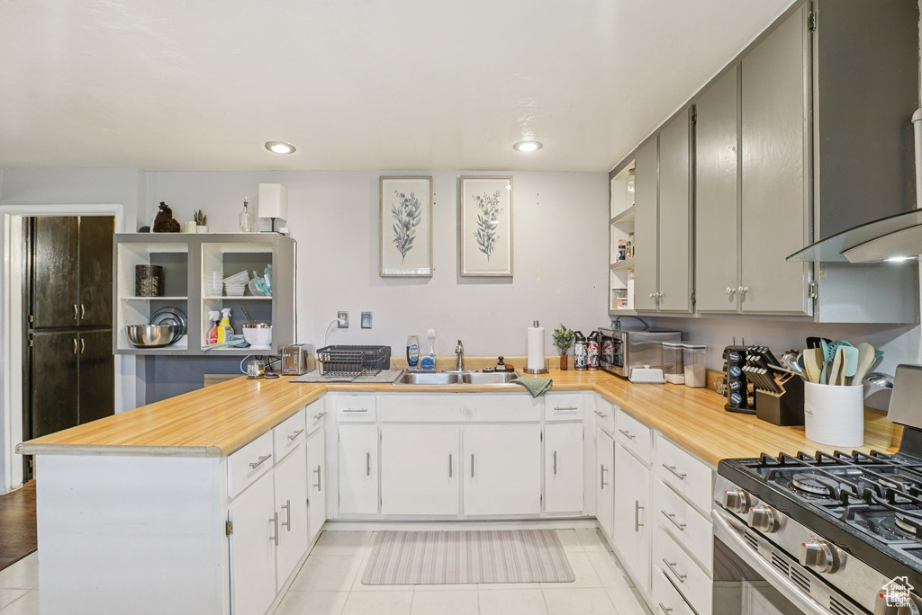 Kitchen featuring stainless steel range with gas stovetop, exhaust hood, a peninsula, open shelves, and recessed lighting