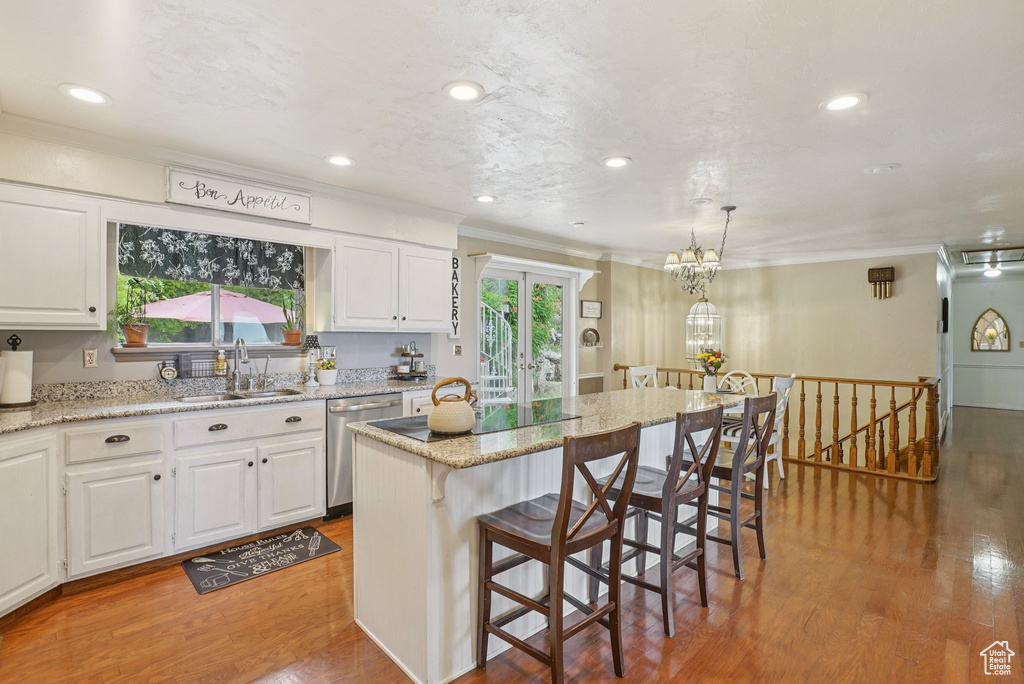 Kitchen featuring stainless steel dishwasher, crown molding, wood finished floors, a breakfast bar, and white cabinetry